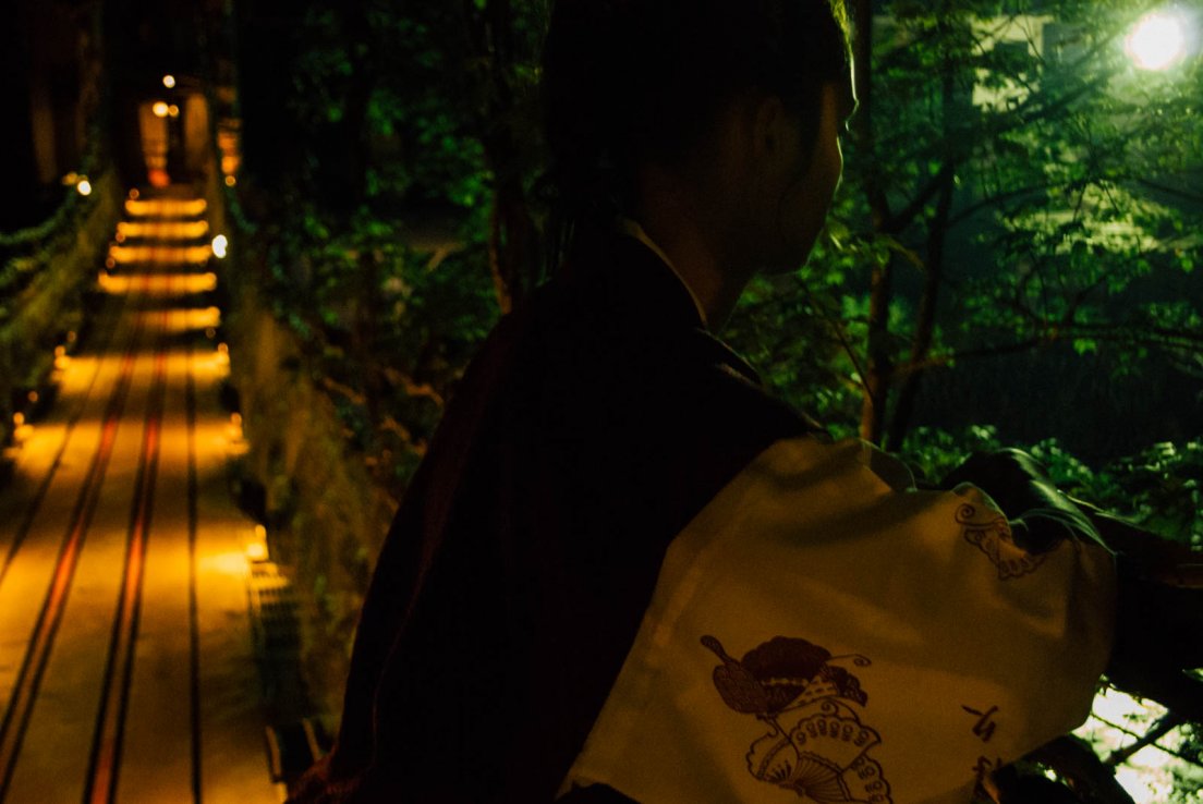 Backlit western girl in a yukata watching over a river bridge by night