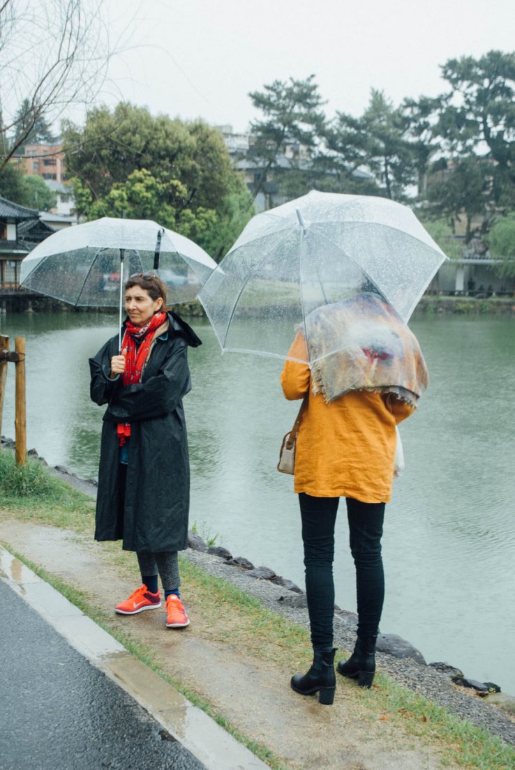 A mother and grown-up daughter standing by a pond holding typically japanese transparent umbrellas