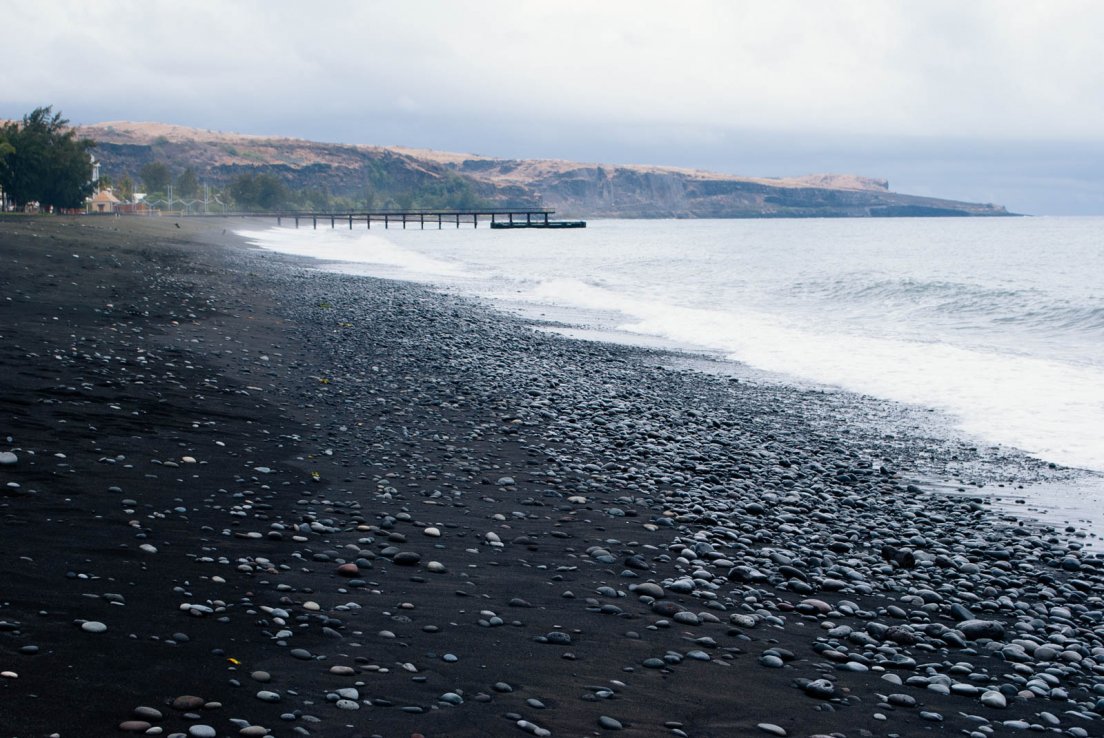 Black sand beach of Saint Paul with a pier lingering in the background by a stormy weather day