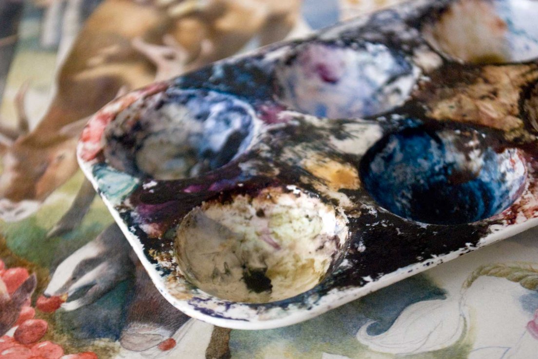 A palette used for watercolour and colored inks with an illustration in the background