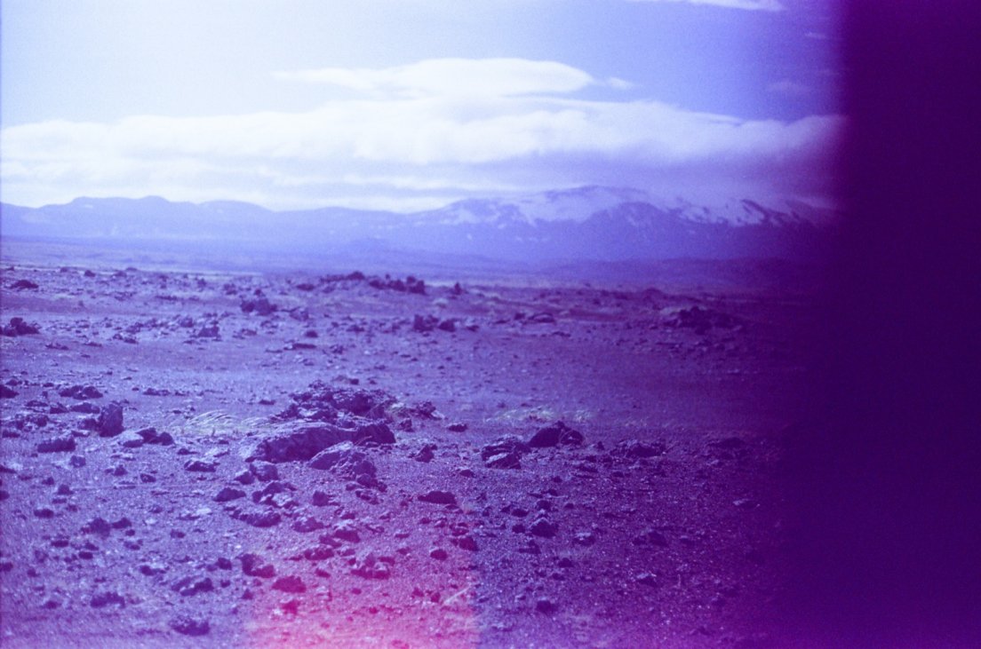 Purple-tinted photograph of the ash and lava desert in front of the volcano
