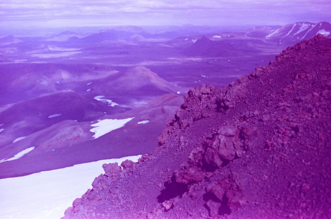 Purple-tinted photograph from the summit of the volcano of the area with patches of snow in the background