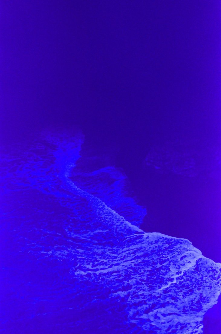 Heavily blue-tinted photograph of the shoreline as seen from the cliff