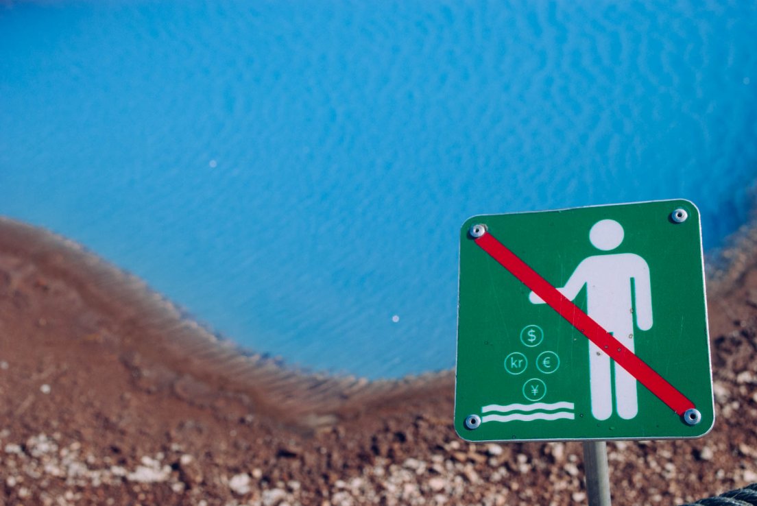 Sign to indicate interdiction of throwing coins above a turquoise geothermic natural pool