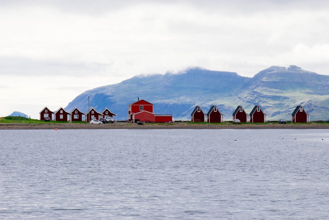 Range of small red wooden cabins by the sea with mountains in the background in the town of Eskifjörður