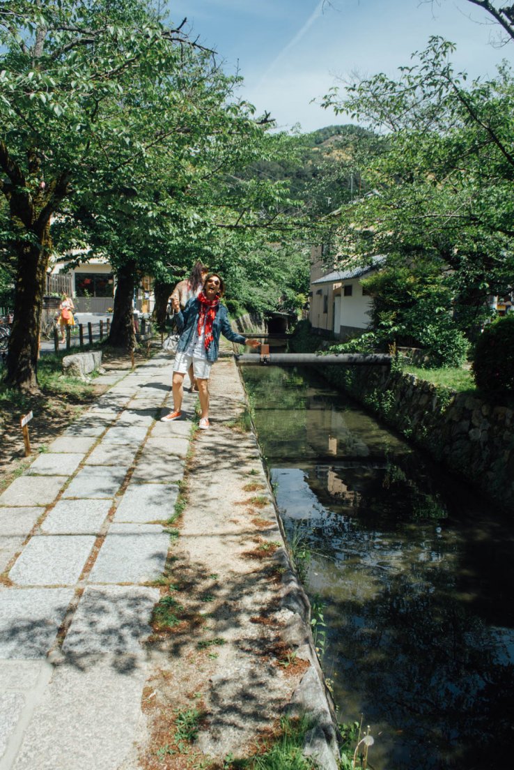 A western lady with a denim jacket and red scarf is fooling around next to the canals on a sunny day