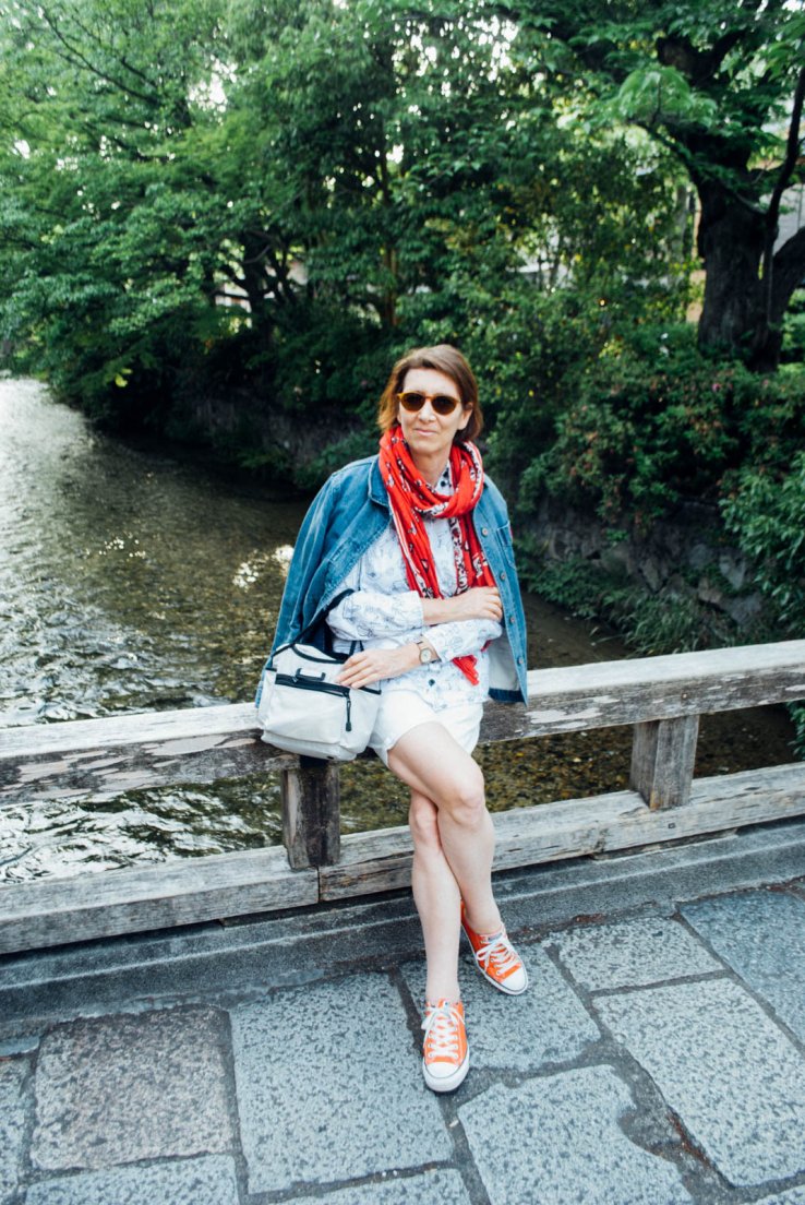 A western woman with a denim jacket and red scarf is sitting on a bridge over a canal, First day in Kyoto #050, Gion Tatsumi bridge, Kyoto, Japan, 08 may 2016 A western woman with a denim jacket and red scarf is sitting on a bridge over a canal