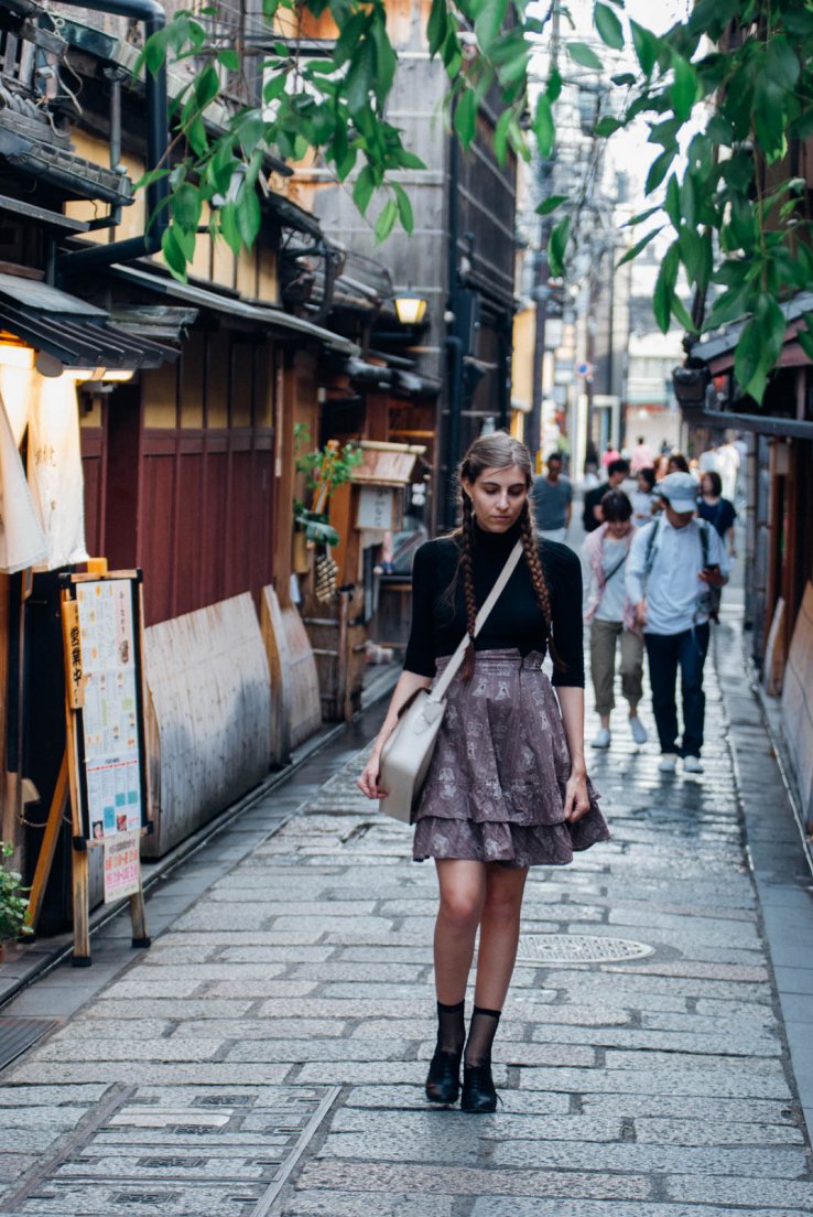 Streetsnap of a western girl with braids, a cream leather satchel, a black top and an Innocent World chess pattern skirt