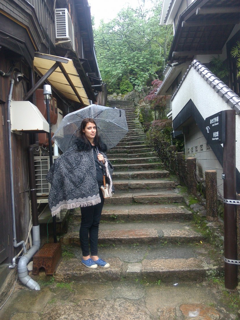 Girl with a poncho and a transparent umbrella standing on the stairs of a narrow street