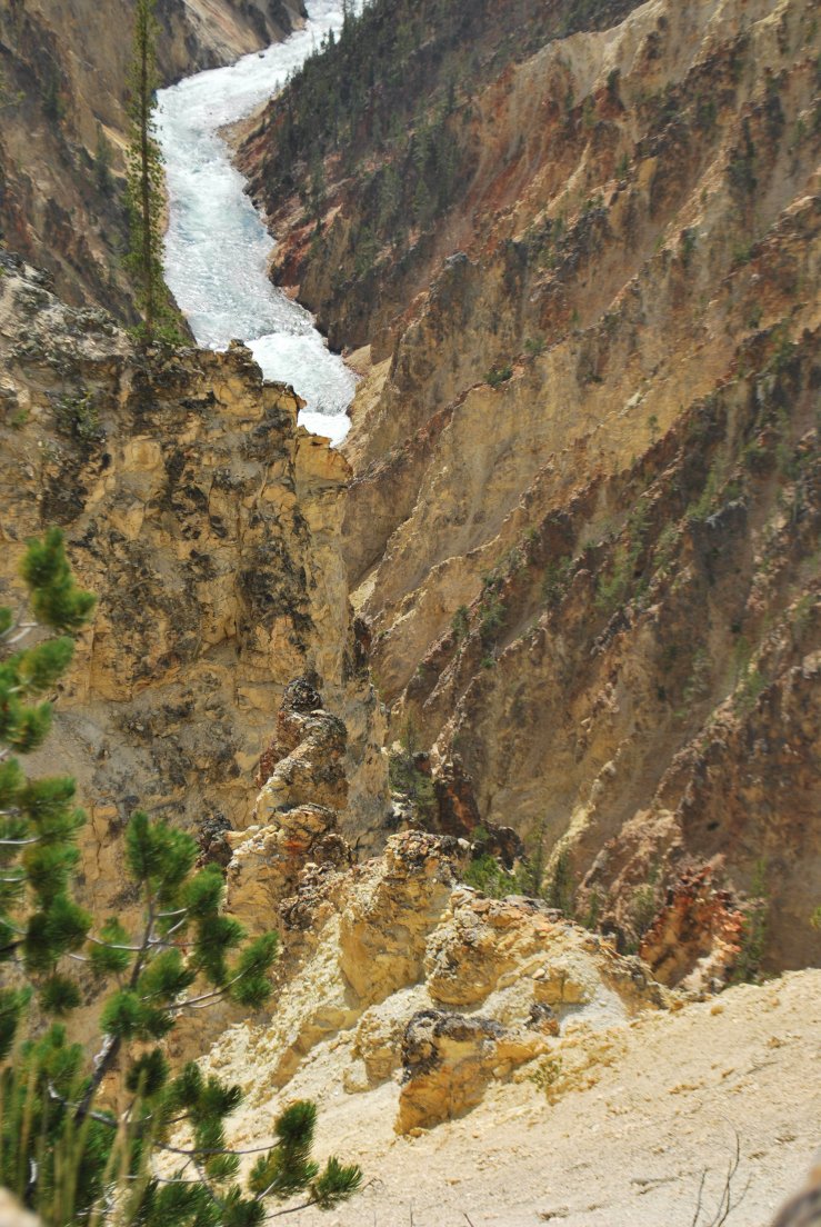 Multi-colored hoodoos in pinks and yellows in a sunny canyon with a waterfall in the background