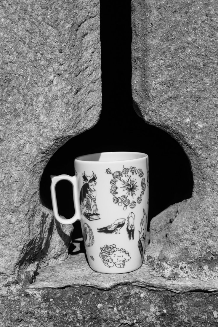 Black and white photograph of a mug from Enchanteresse, a collection of hand-painted porcelains by messalyn, on the windowsill of an arrowslit
