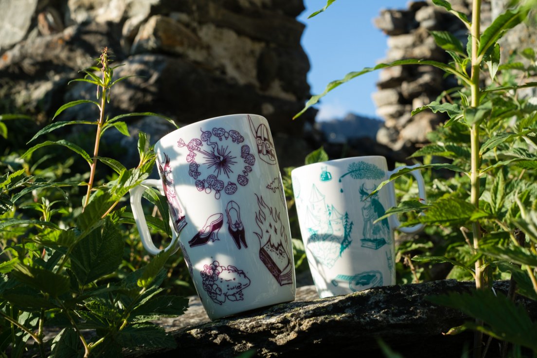 Purple and seafoam mugs from Enchanteresse, a hand-painted porcelain collection by messalyn, standing amongst the ruins of an abandoned village in the mountains