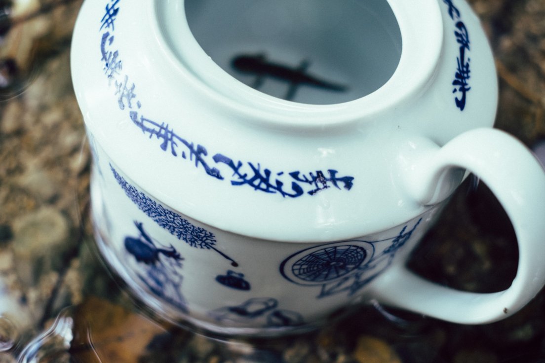 A blurry salamander resting at the bottom of a hand-painted teapot from the Enchanteresse collection, centered around the faery realm