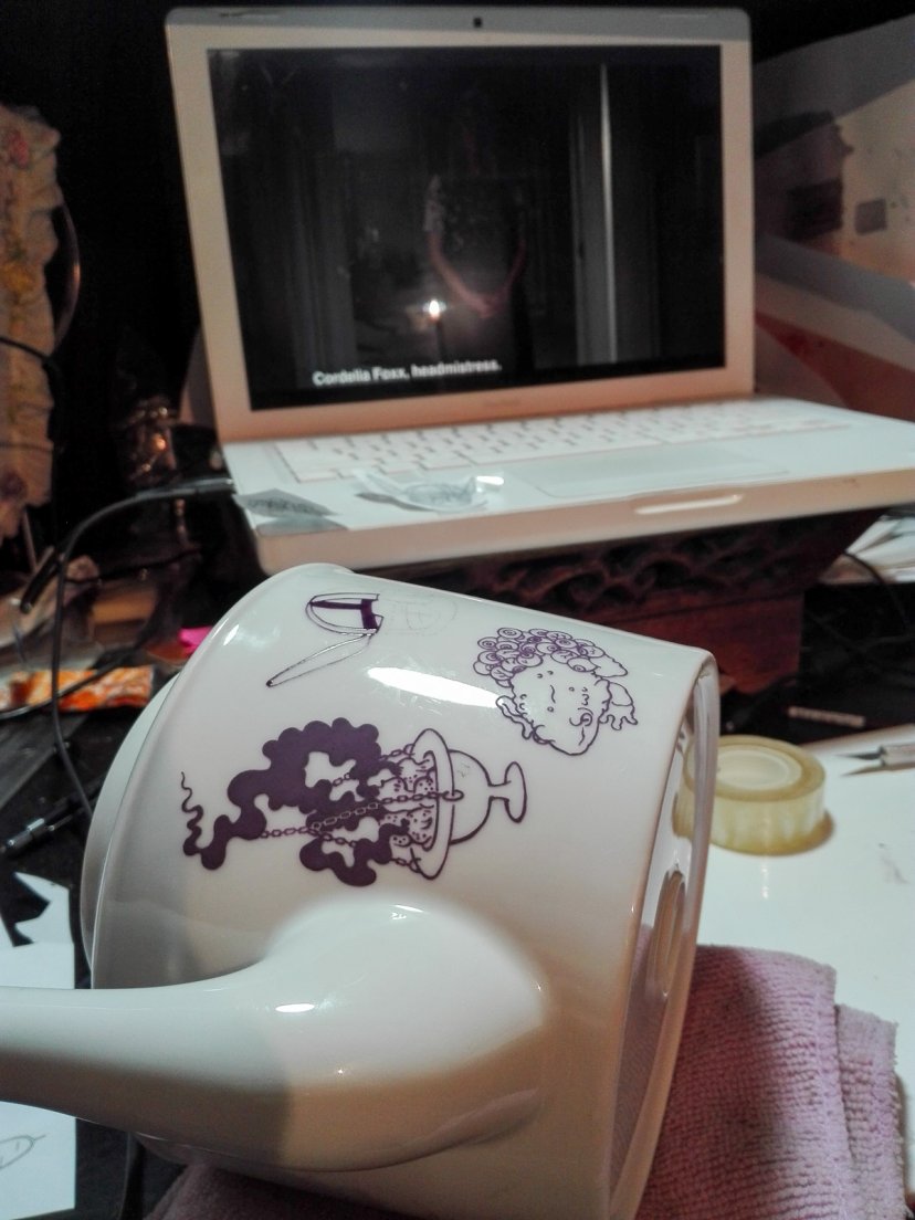 Work in progress of a purple teapot from Enchanteresse, a hand-painted porcelain collection by messalyn, in front of the tv show American Horror Story: Coven