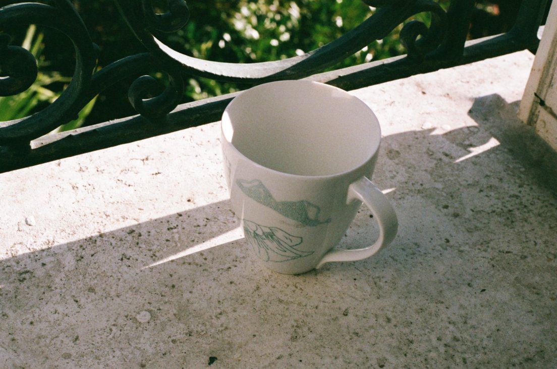 Analog photo of a large teacup in the process of being painted with a lingerie theme in seafoam green, but still unfired